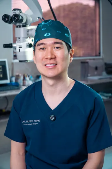 Dr. Hugo Araki de traje cirúrgico ao lado do microscópio de cirurgia refrativa